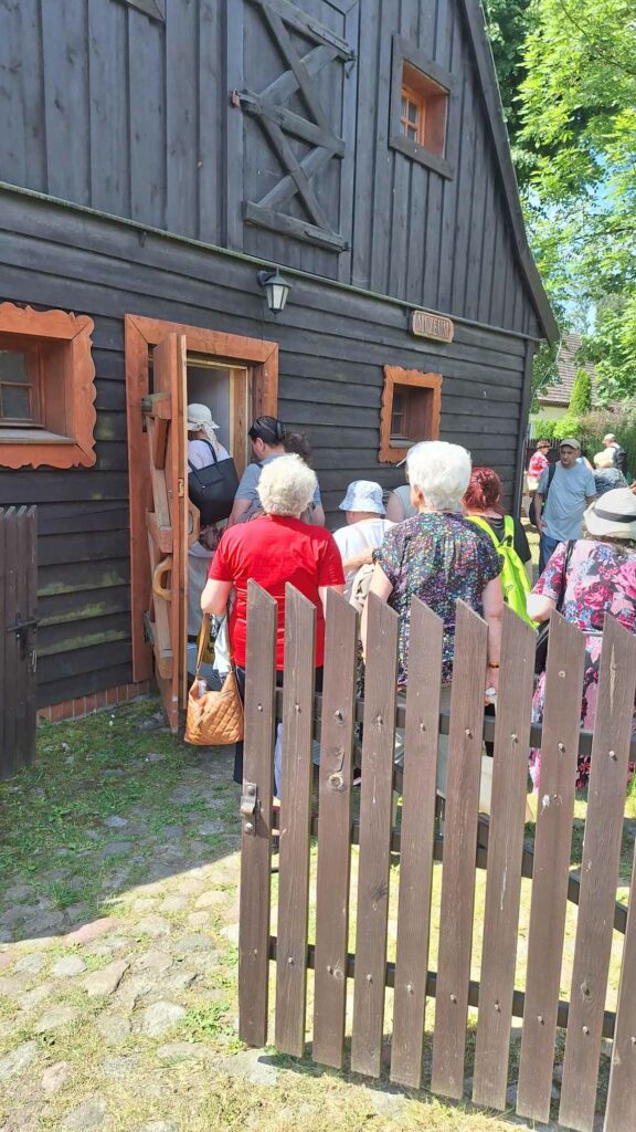 Uczestnicy wchodzą do drewnianego budynku z tabliczką muzeum