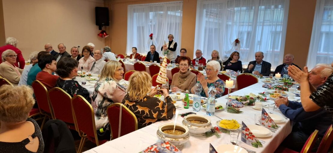 Kilka zastawionych stołów przy środkowym z nich Pani siedząca w rogu ogląda otrzymaną choinkę jako nagrode w konkursie.